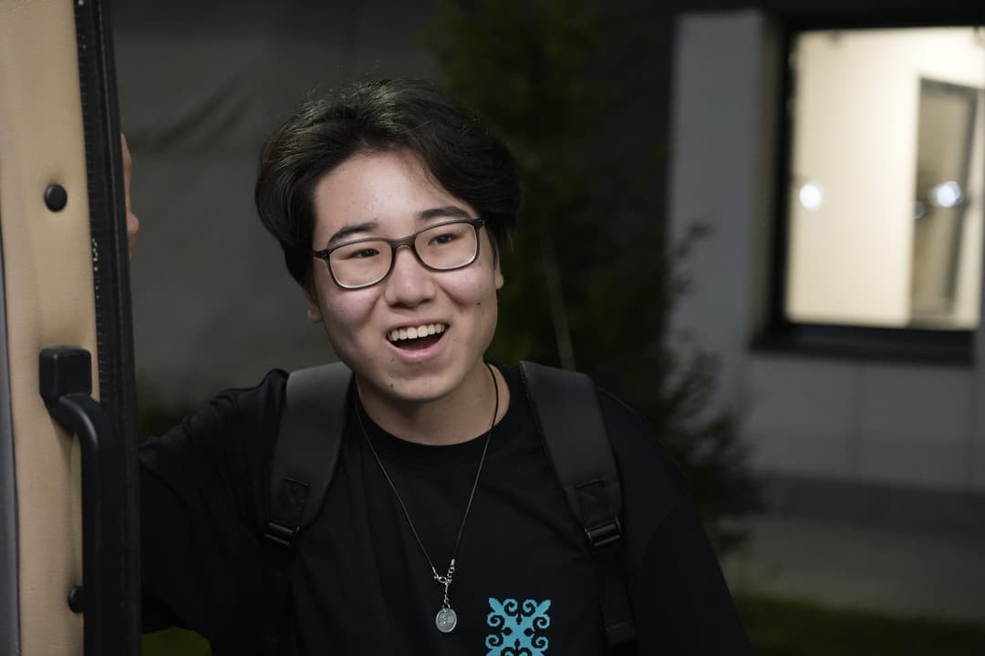 Portrait of Ali laughing in the dormitory doorway at night, backpack over one shoulder