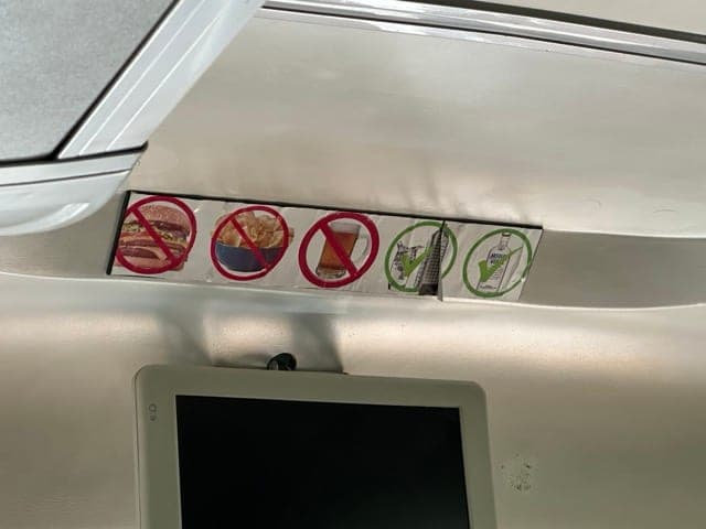Row of pictogram signs above a bus window: hot food, chips and drinks crossed out; only bottled water allowed