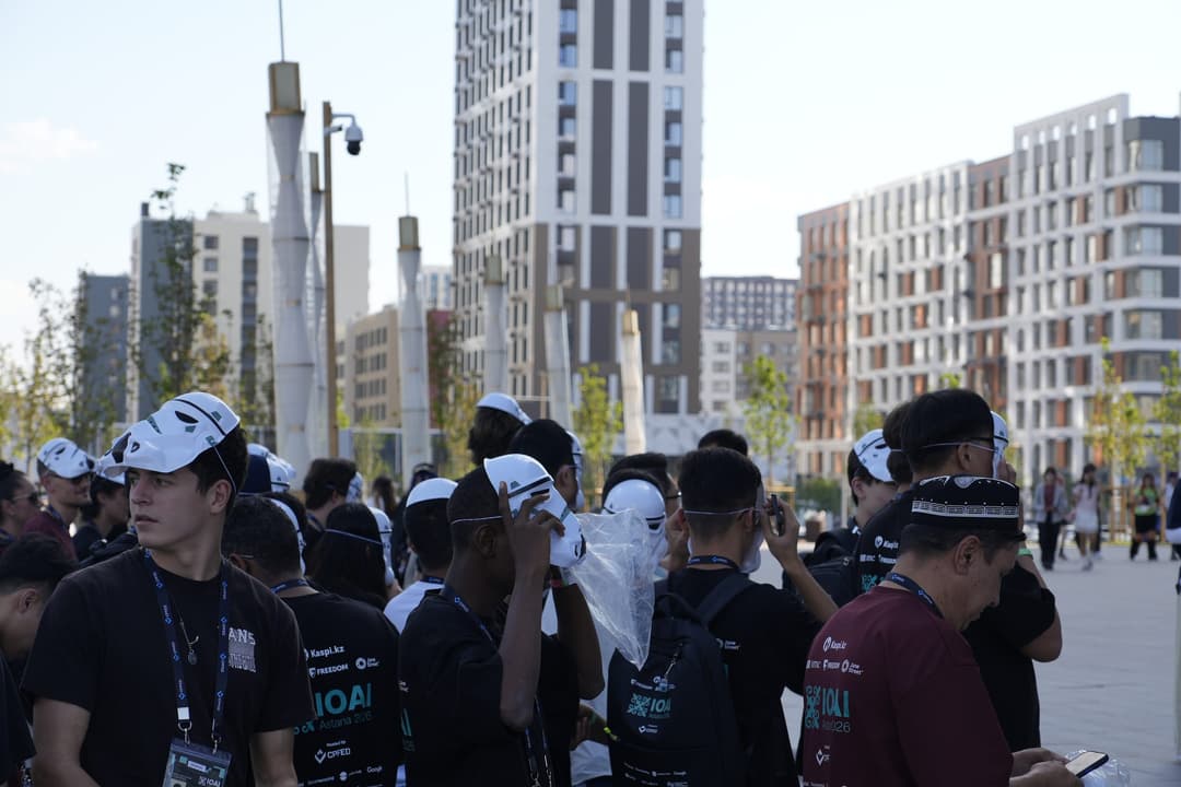A crowd of IOAI contestants outside the Comic Con venue, most wearing white plastic masks pushed up onto their foreheads