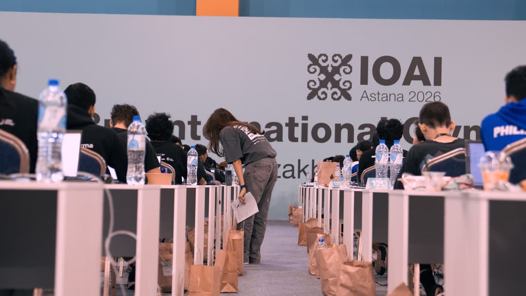 Rows of individual desks with contestants working at laptops in front of a large IOAI Astana 2026 banner