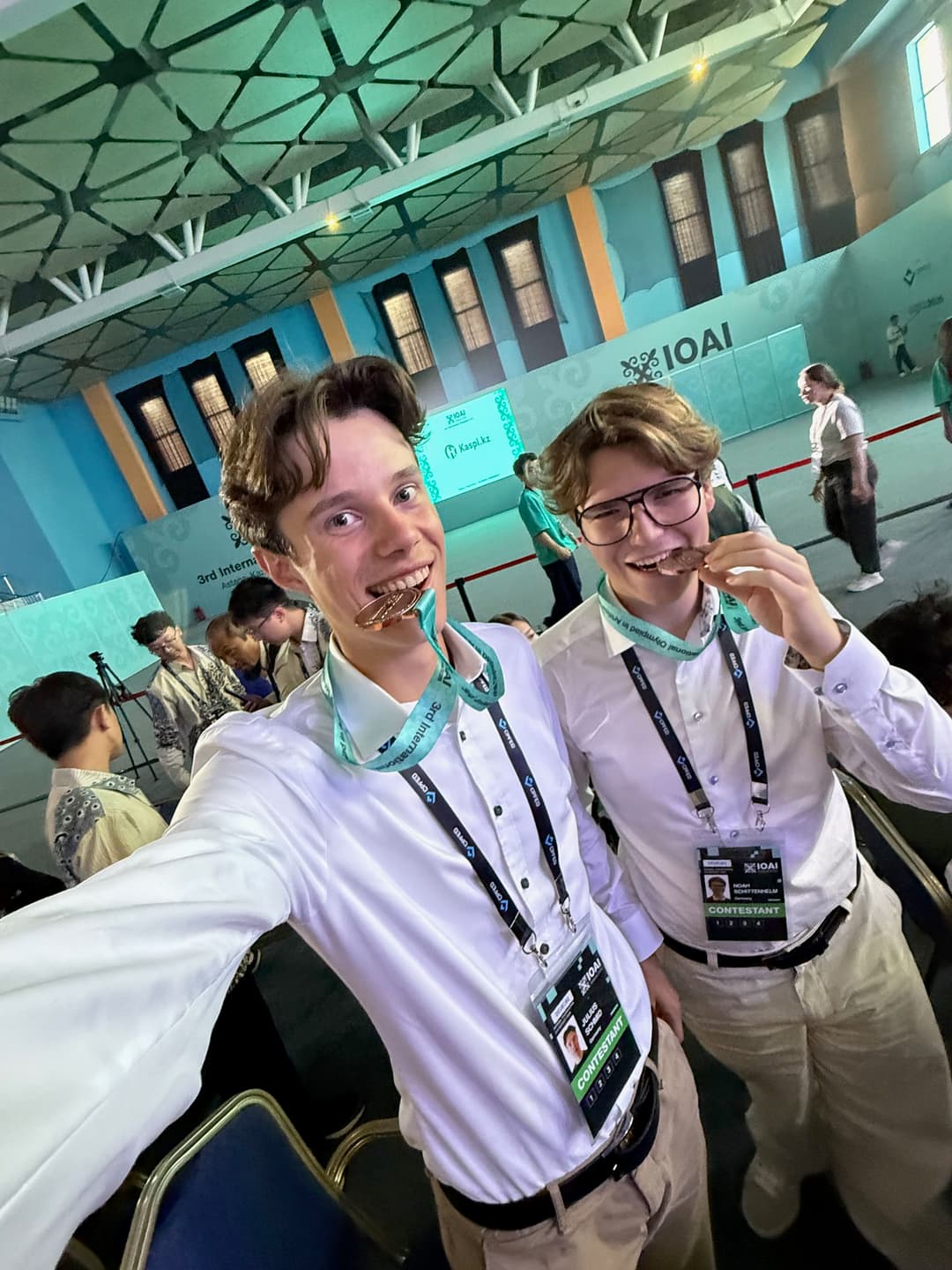 Selfie of two team members pretending to bite their bronze medals in the venue
