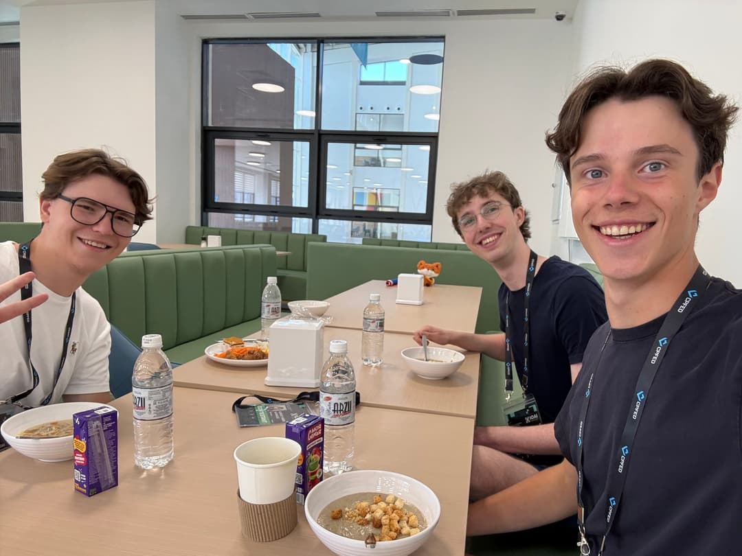 Three team members smiling around a cafeteria table with bowls of soup, water bottles and juice cartons
