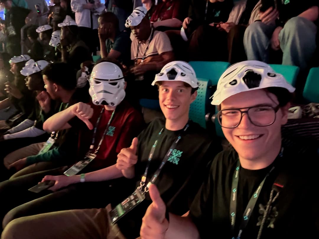 Selfie of three team members inside a dark event hall wearing white Stormtrooper-style masks tilted up