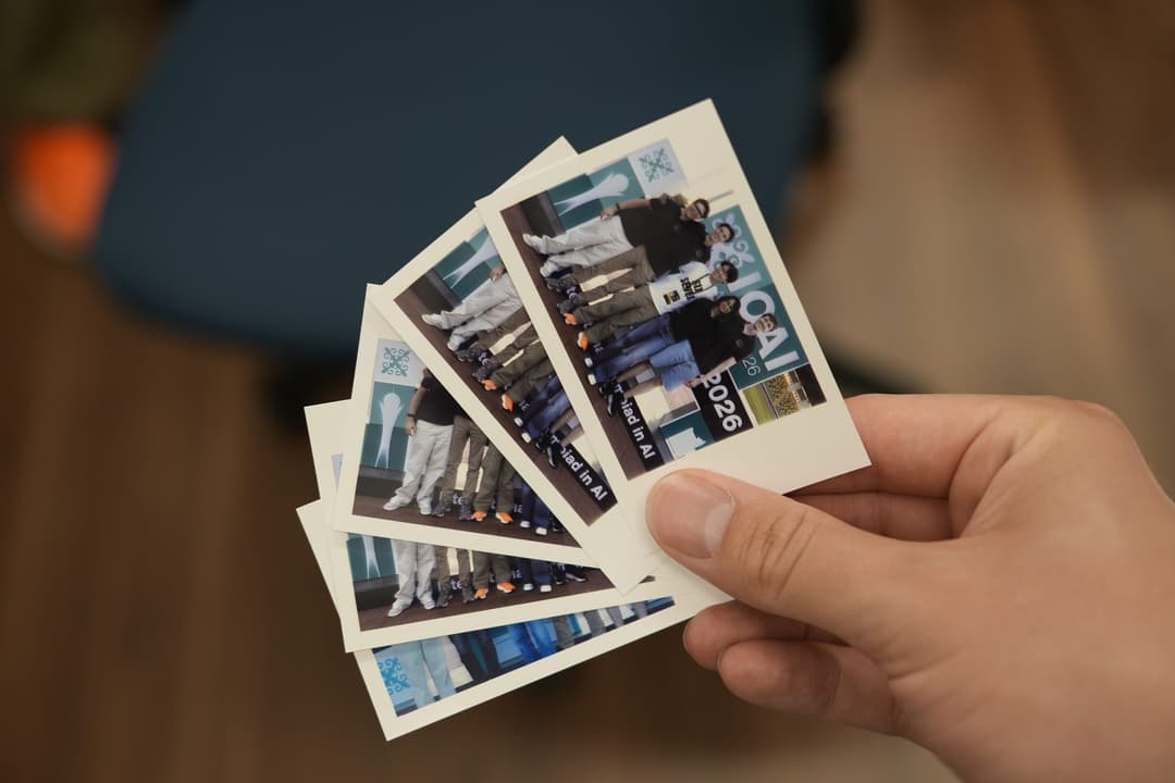 A hand holding a fan of six Polaroid photos of Team Germany taken in front of an IOAI backdrop
