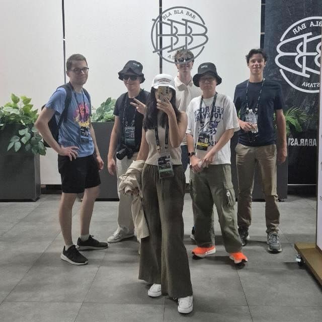 Group mirror selfie of six friends posing in front of a bar wall in Astana