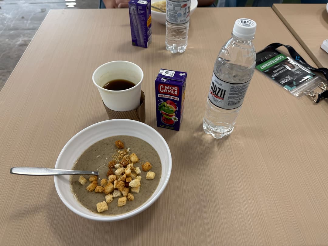 Bowl of grey mushroom soup topped with croutons, next to a coffee cup, a juice carton and a bottle of water