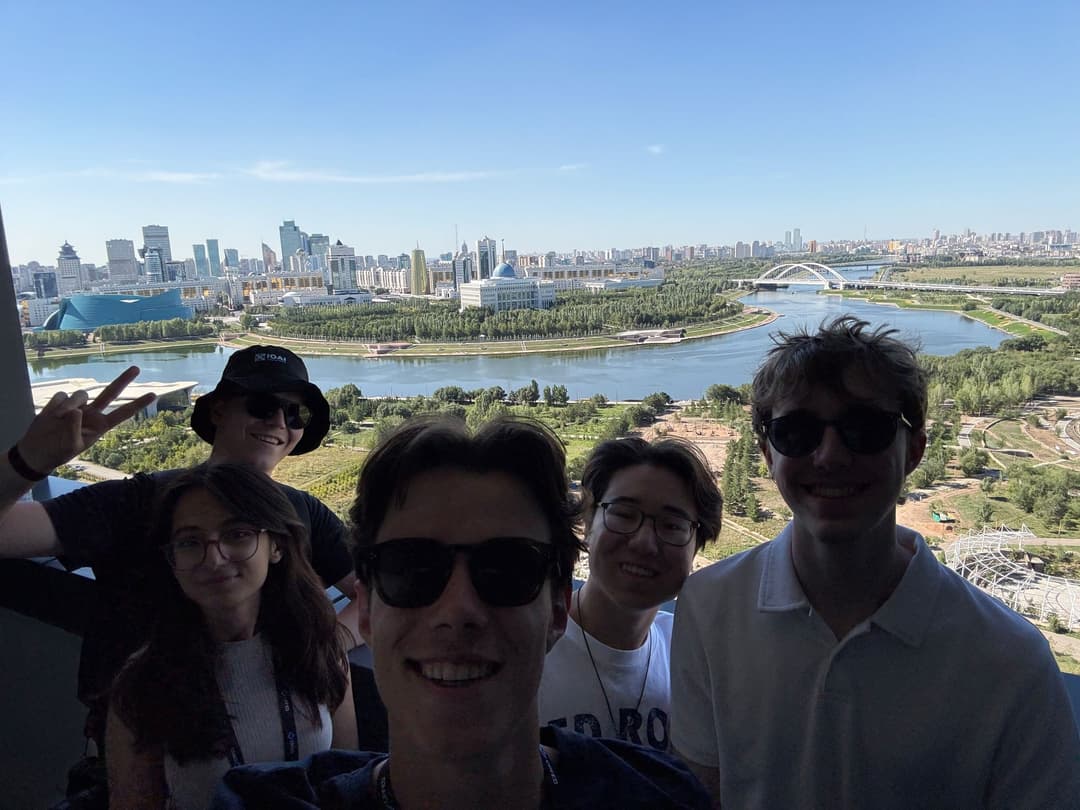 Group selfie of five people on a viewing platform, with the Ishim river and the Astana skyline in the background